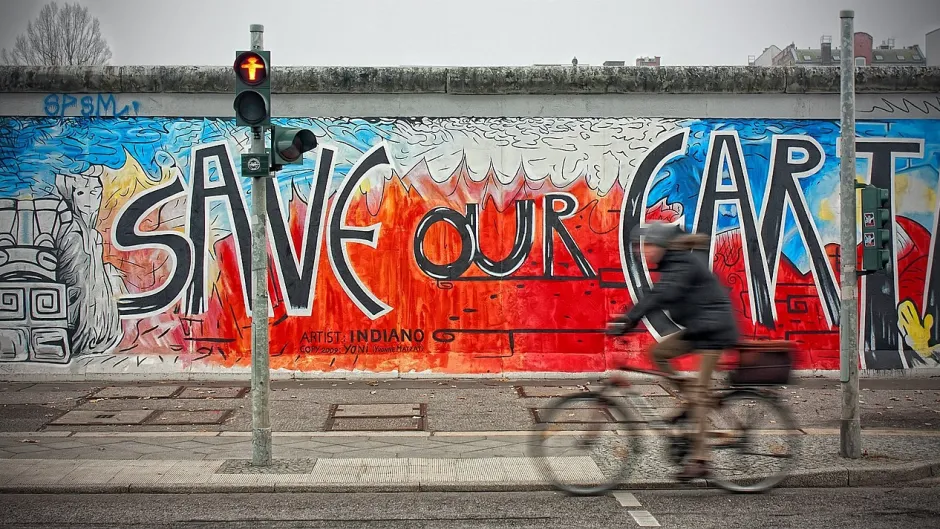 Blick auf die Graffiti-besprühte Berliner Mauer hinter einer roten Fußgängerampal: Save Our Earth